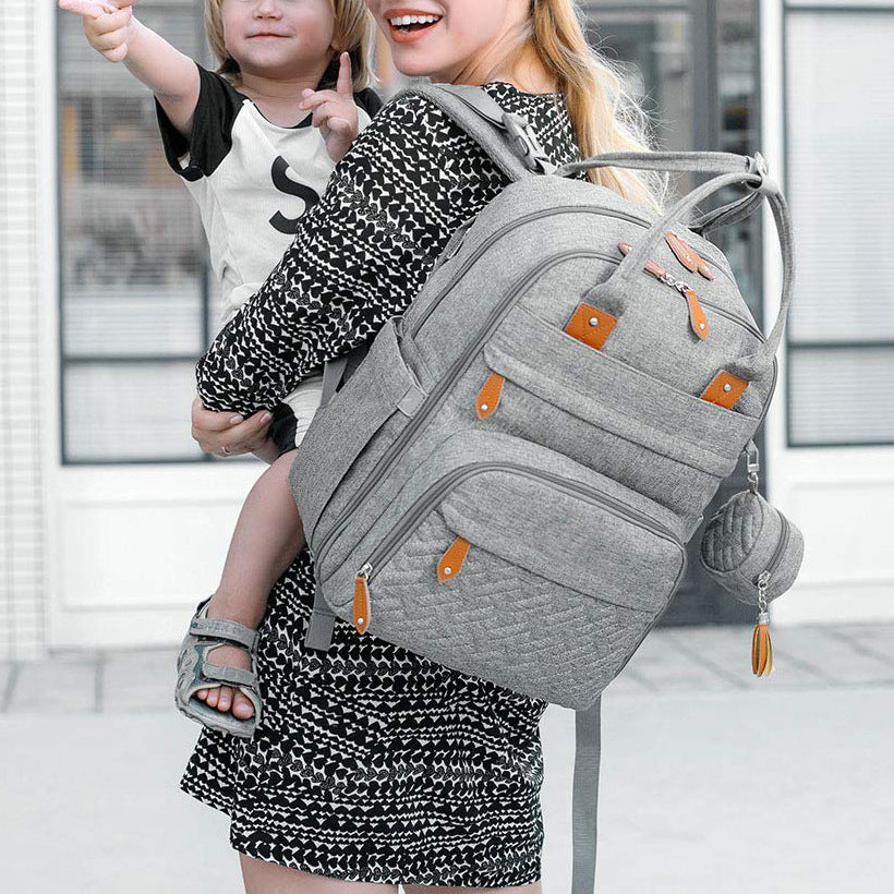 Mum carrying child while wearing stylish grey nappy bag backpack